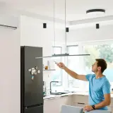 Mężczyzna z pilotem przy klimatyzatorze w nowoczesnej kuchni.