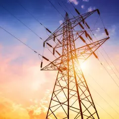 Słup energetyczny na działce, zasilający dom. Zachód słońca maluje niebo na pomarańczowo i niebiesko.