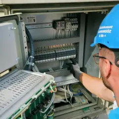 Elektryk w niebieskim kasku pracuje przy panelu sterowania, przygotowując oświadczenie o gotowości instalacji przyłączanej.