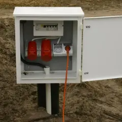 Skrzynka elektryczna na działce bez domu, gotowa na podłączenie prądu. Widoczne zabezpieczenia i gniazda.