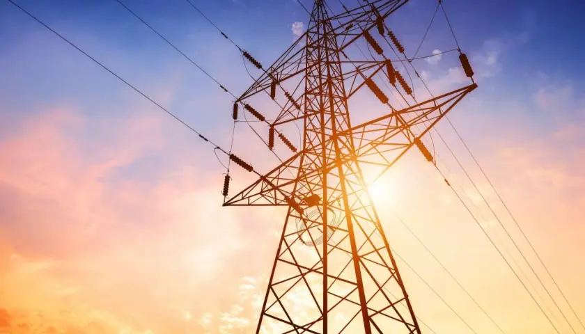 Słup energetyczny na działce, zasilający dom. Zachód słońca maluje niebo na pomarańczowo i niebiesko.