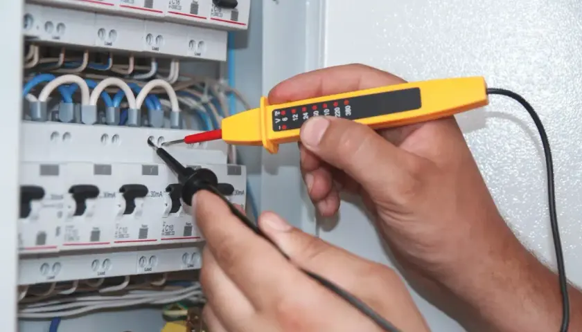 Elektryk sprawdza napięcie w skrzynce bezpieczników. Miernik wskazuje moc pozorną, pomagając zapewnić bezpieczeństwo instalacji.