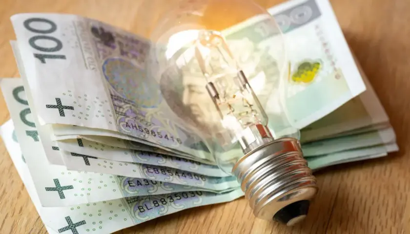 Żarówka na stosie banknotów 100 zł symbolizuje wysokie rachunki za prąd.