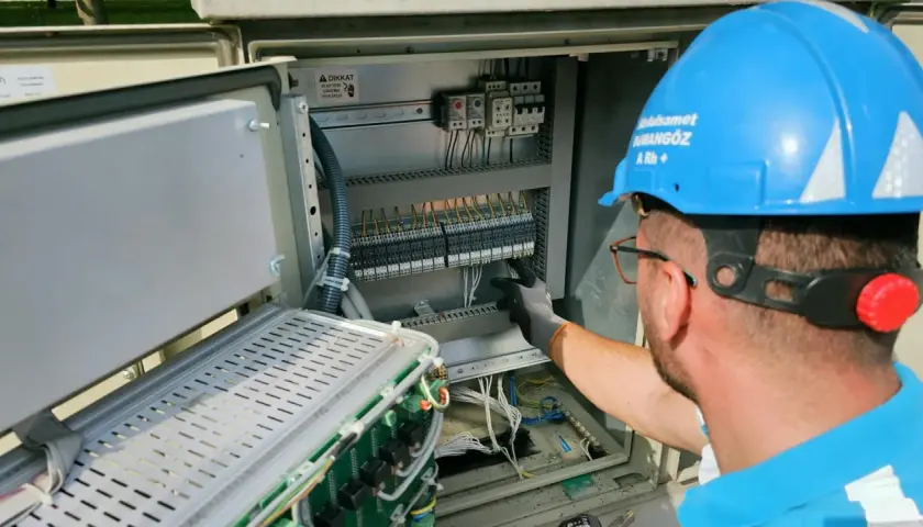 Elektryk w niebieskim kasku pracuje przy panelu sterowania, przygotowując oświadczenie o gotowości instalacji przyłączanej.
