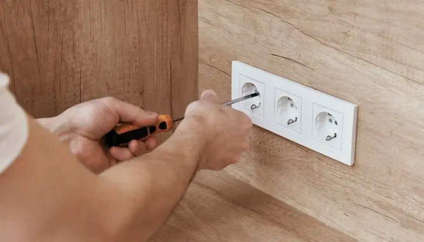 Ręce majsterkowicza przykręcają gniazdko. Dbałość o detale zapewnia bezpieczne napięcie skuteczne w domu.
