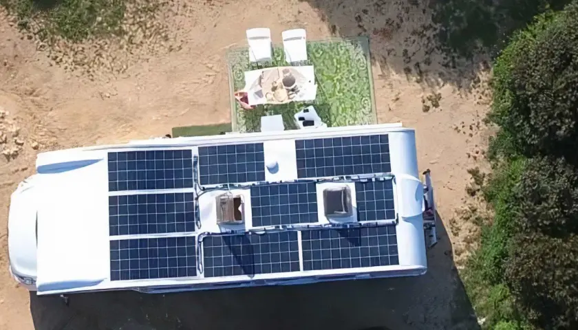 Kamper z panelami słonecznymi na dachu, idealny do życia w stylu instalacja off grid. Na zewnątrz stolik z kawą i krzesła.