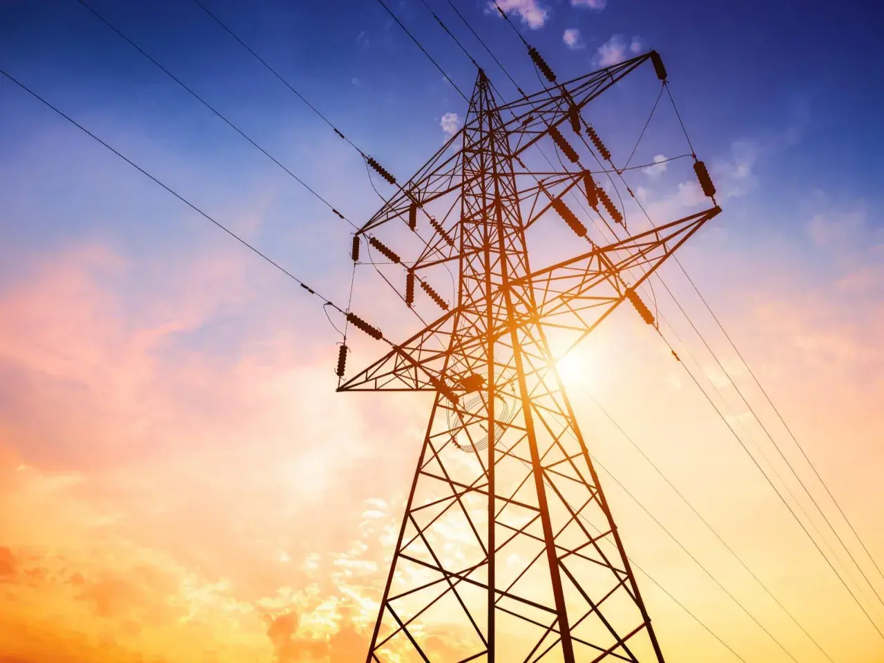 Słup energetyczny na działce, zasilający dom. Zachód słońca maluje niebo na pomarańczowo i niebiesko.