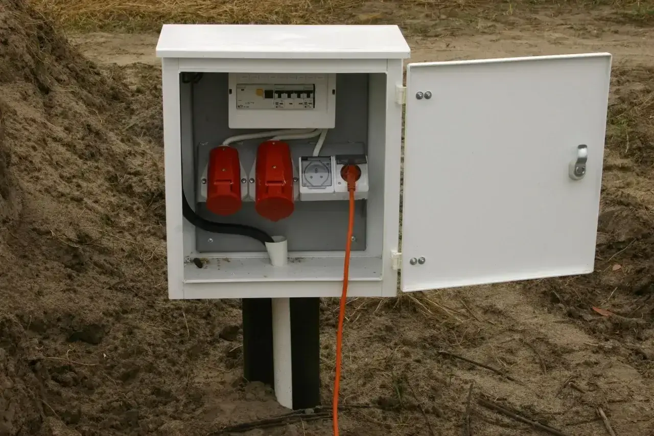 Skrzynka elektryczna na działce bez domu, gotowa na podłączenie prądu. Widoczne zabezpieczenia i gniazda.