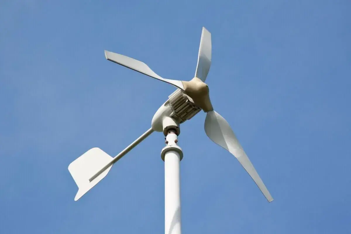 Biała elektrownia wiatrowa z trzema łopatami na tle błękitnego nieba.