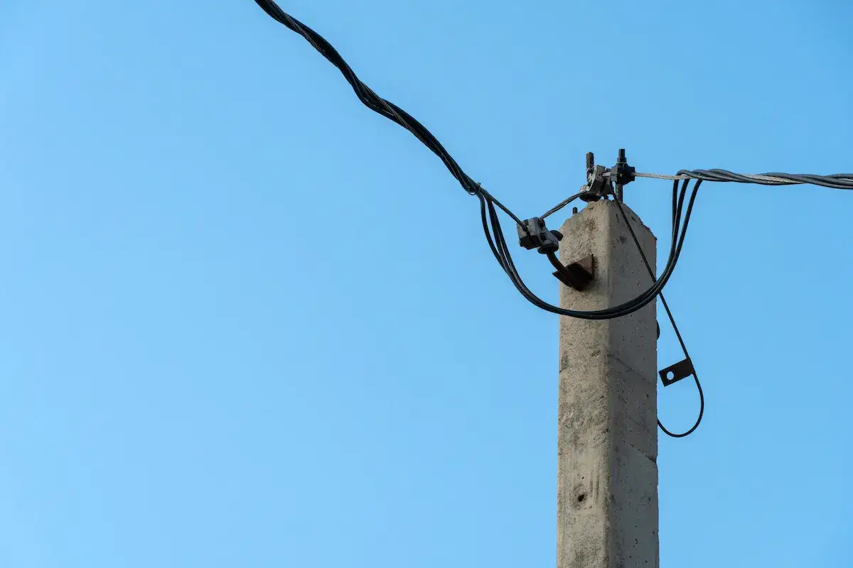 Betonowy słup energetyczny z przewodami na tle błękitnego nieba. Zastanawiasz się, ile za słup energetyczny na działce?