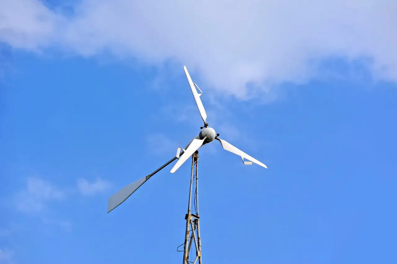 Białe turbiny wiatrowe obracają się na tle błękitnego nieba z chmurami.