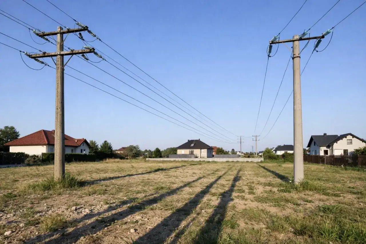 Słupy energetyczne nad polem, domy w tle. Czy można uzyskać odszkodowanie za słupy energetyczne? Forum dyskusyjne może pomóc.